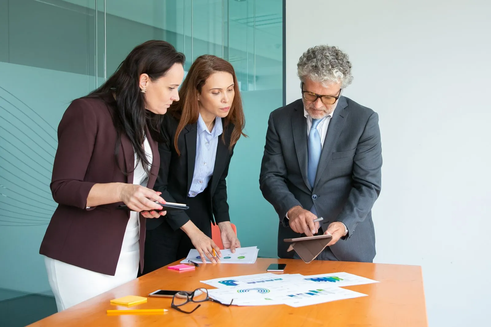 Three colleagues reviewing documents and a tablet together at a meeting table